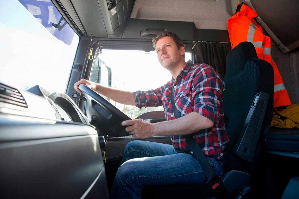 Mies ajaa kuorma-autoa, taustalla roikkuu huomioliivi.