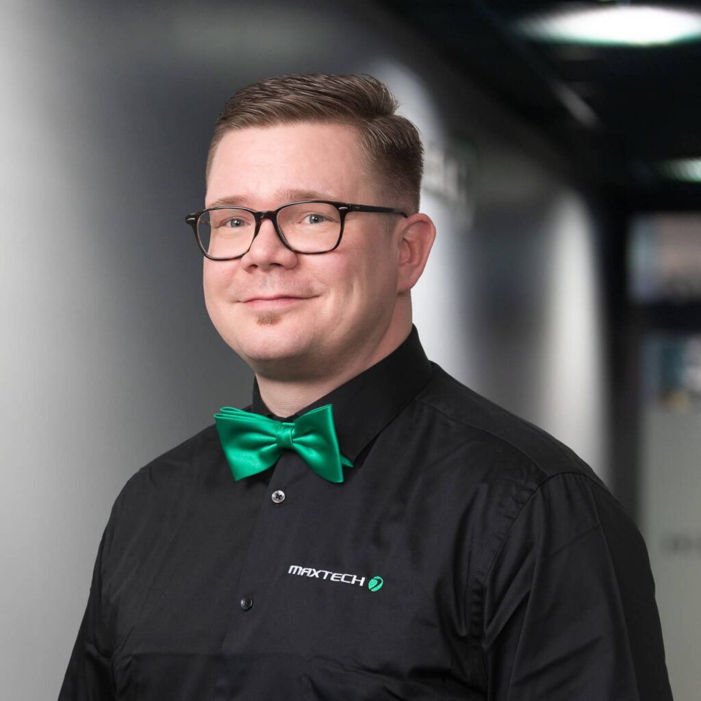 Maxtechin toimitusjohtaja, Mikko Ängeslevä, hymyilee kasvokuvassa vihreä rusetti kaulassa.